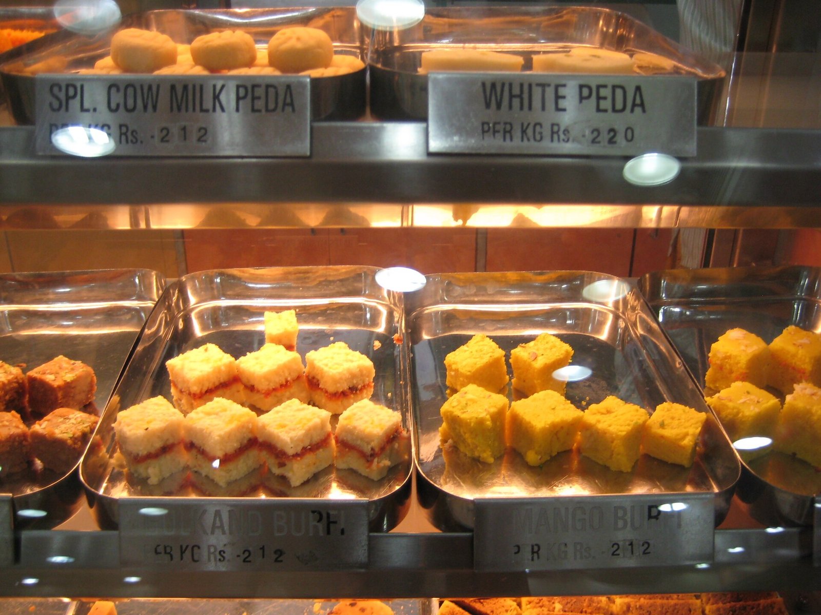Assorted Indian barfi and peda sweets topped with pistachios in a display tray