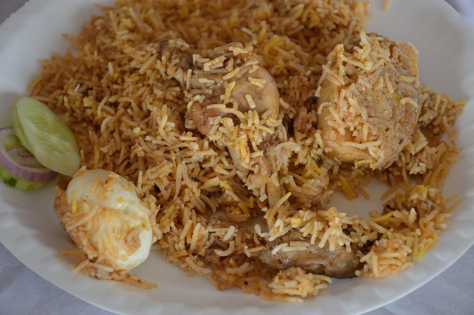 A plate of chicken biryani with saffron rice, fried onions and raita